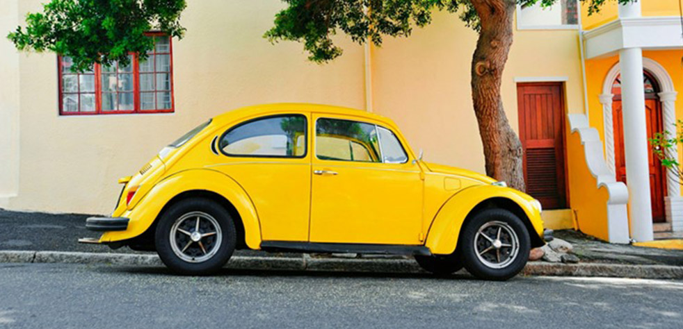 Photo d’une voiture jaune de collection stationnée au bord d’une route