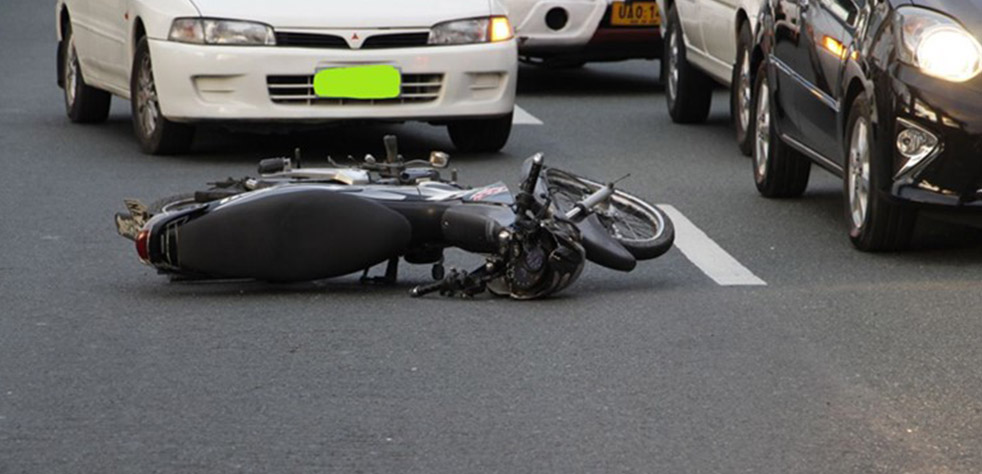 Photo d’une moto couchée sur la route devant une voiture
