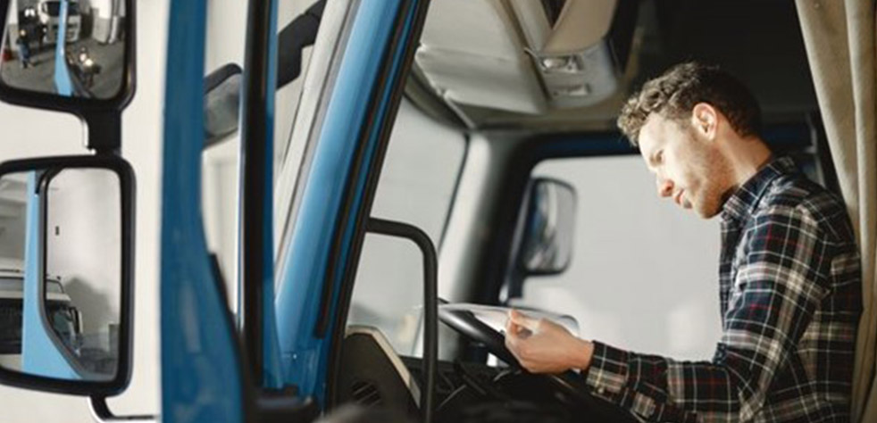 Photo d’un homme assis au volant d’un camion en train de consulter un document