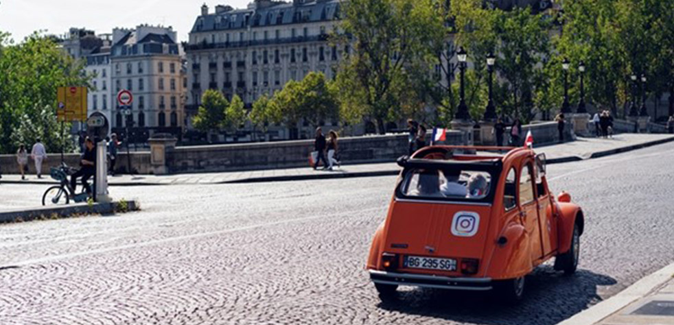 Photo d’une 2CV orange circulant sur une route pavée